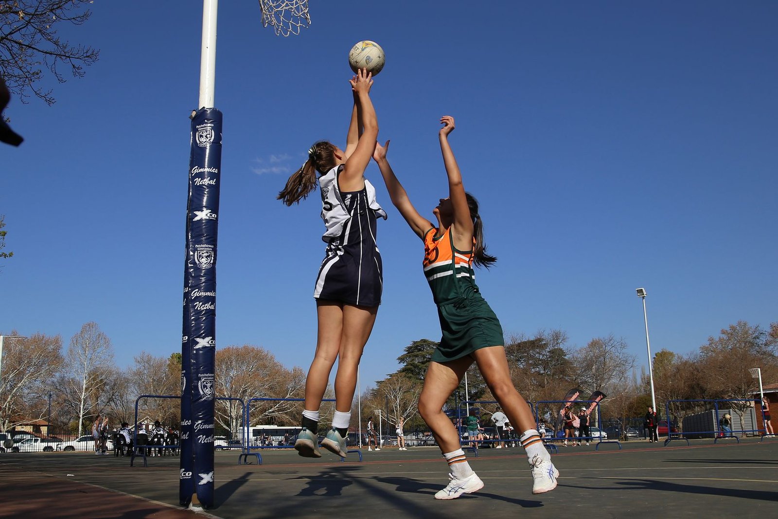 Two netball players contesting a shot beneath the goal ring